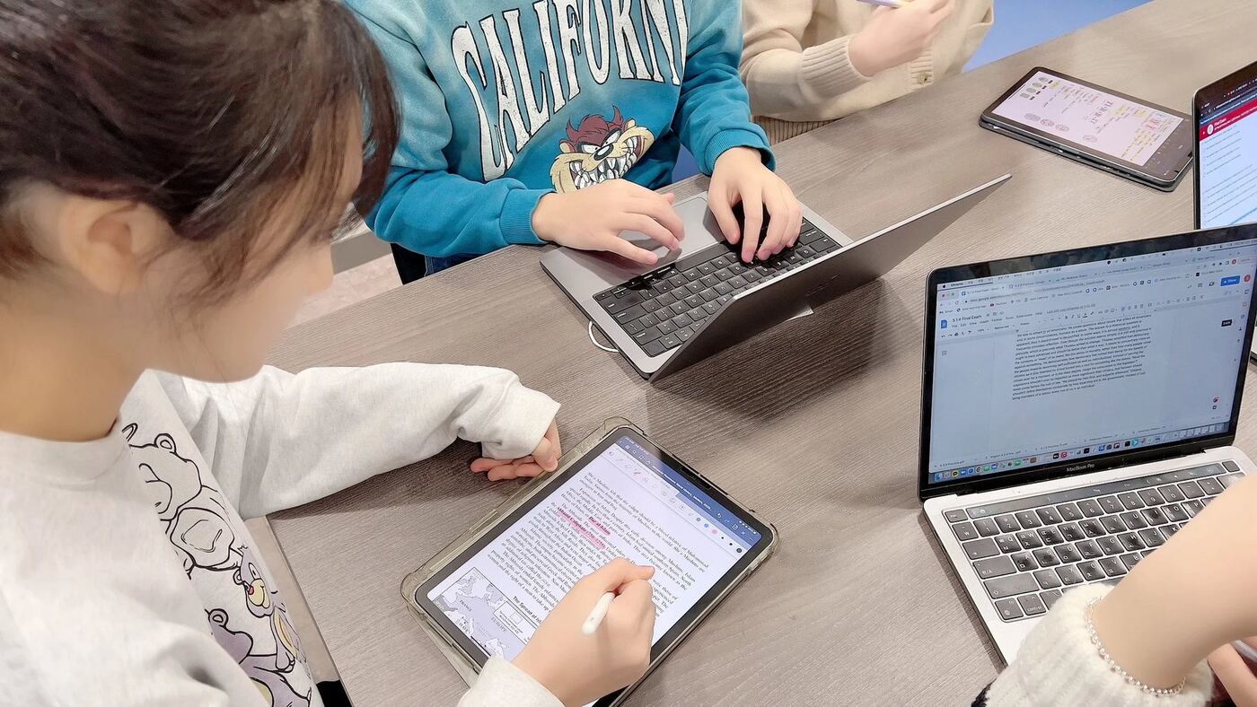 Students annotating readings on tablets and laptops at a shared table